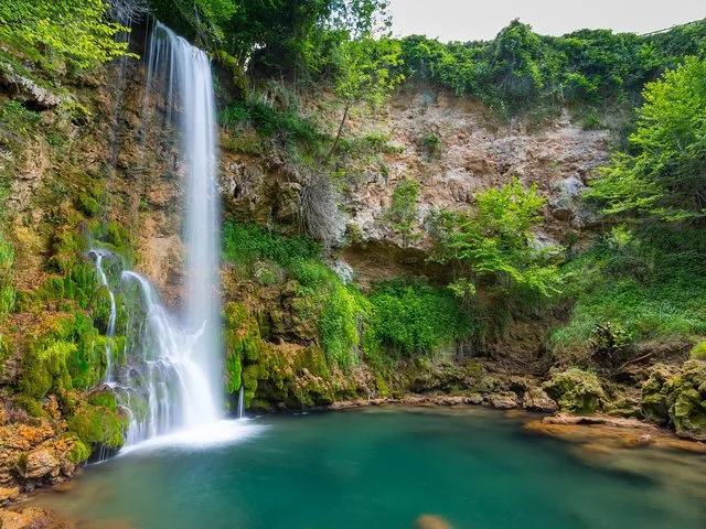 Tall waterfall cascading into a clear turquoise pool surrounded by greenery