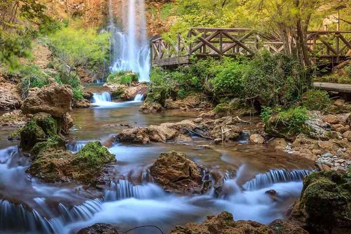 Arroyo que cae sobre las rocas cerca de un puente de madera y una cascada