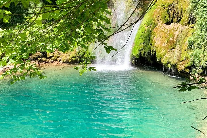 Clear turquoise pool at the base of a rocky, moss-covered waterfall